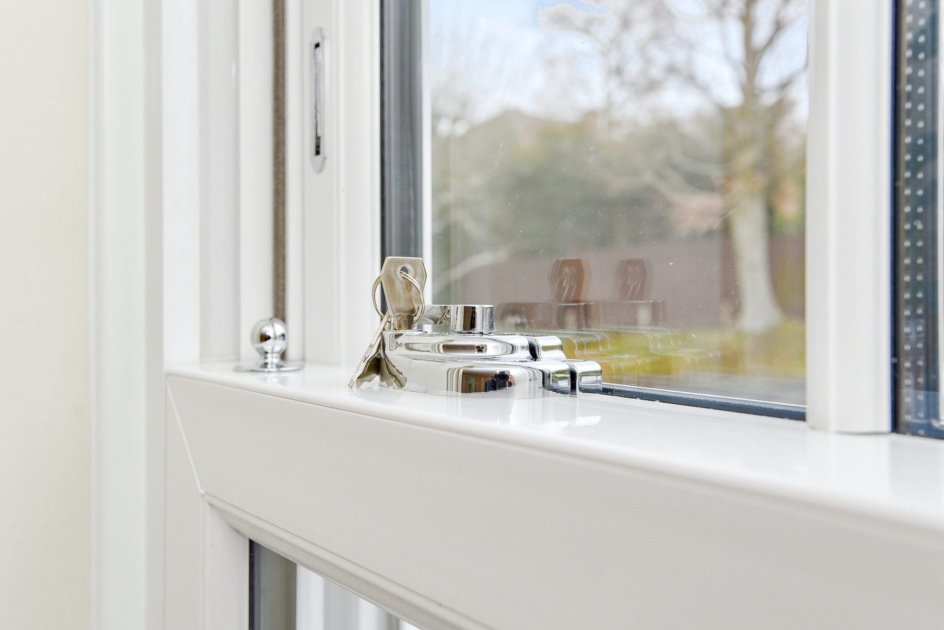 Close up photo of a crystal clear view through a Victorian Sliding Sash window with a key in the lock. Image depicts a guarantee of quality. A photo by Three Counties glazing.
